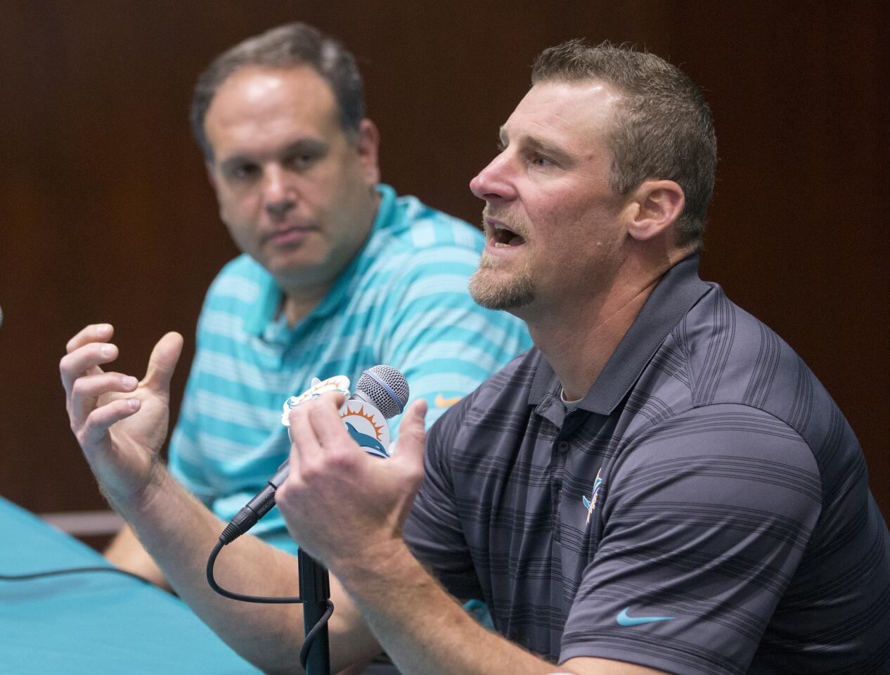 Former Miami Dolphins tight ends coach Dan Campbell, foreground, gestures as he speaks during a news conference after being promoted to interim head coach, Monday, Oct. 5, 2015 in Davie, Fla. At rear is Mike Tannenbaum, left, Miami Dolphins executive vice president of football operations. Joe Philbin has been fired four games into his fourth season as coach of the Miami Dolphins, and one day after a flop on an international stage that helped to seal his fate. (AP Photo/Wilfredo Lee)