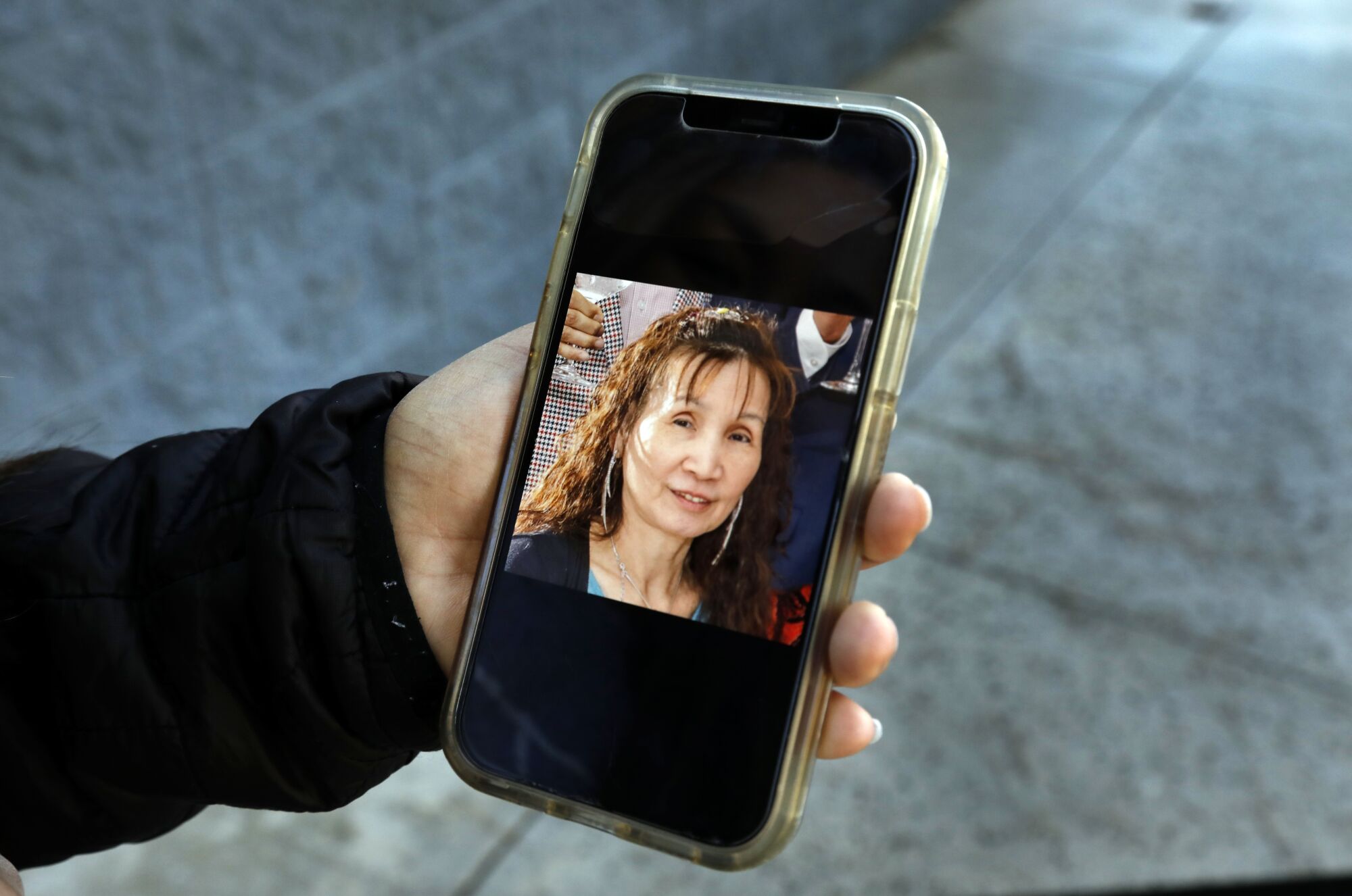 A hand holding a phone with a portrait of an Asian woman lightly smiling.