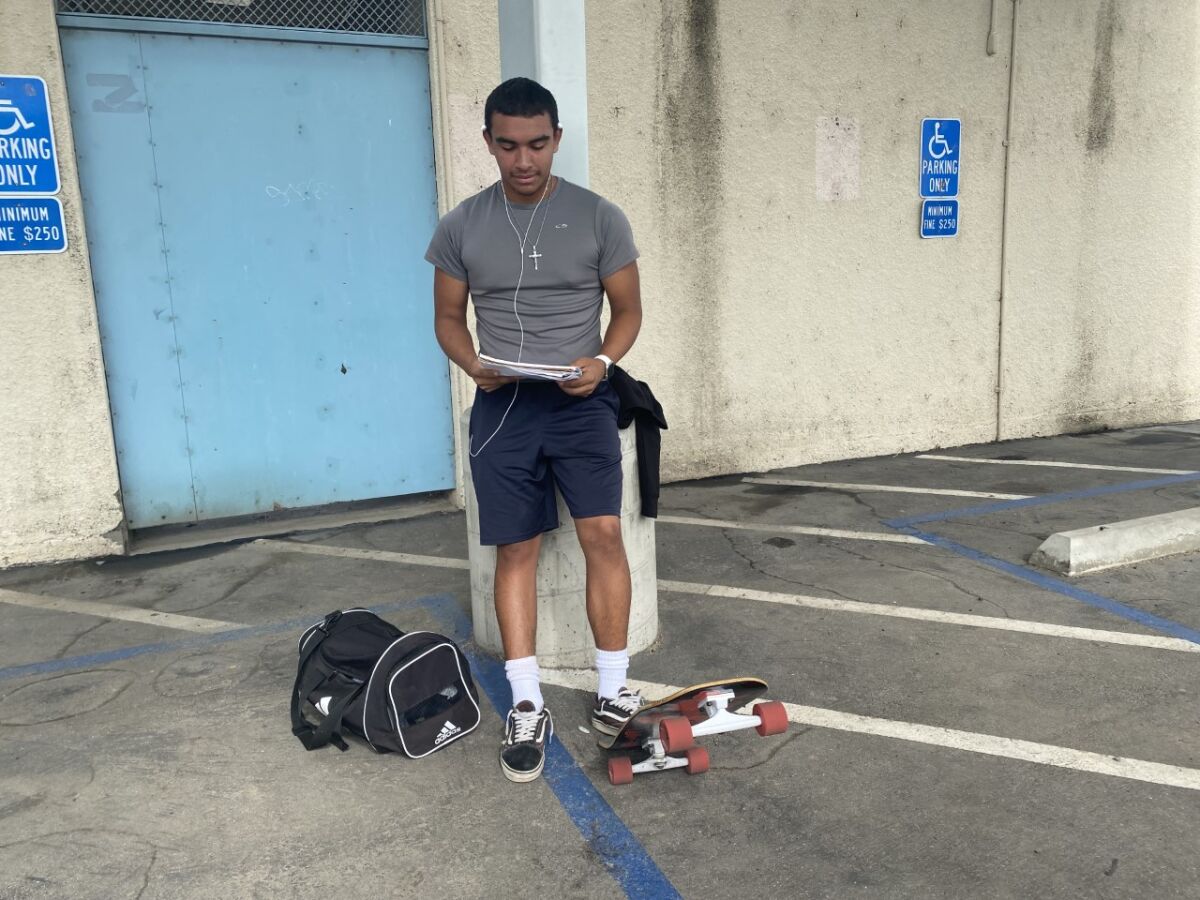 Daniel Najar stands with one foot on his tipped up skateboard.
