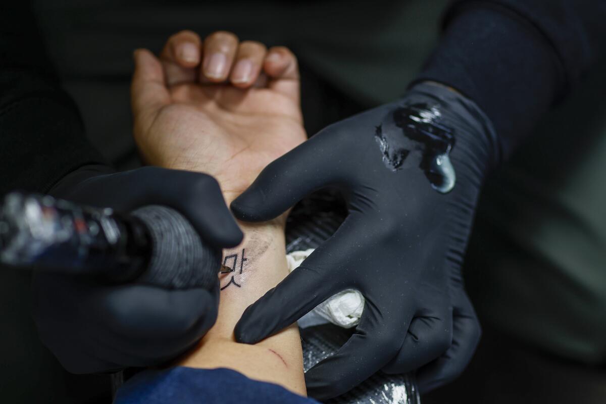 Tattoo artist tattoos the Korean symbol for "taste, savor, flavor" on a wrist.