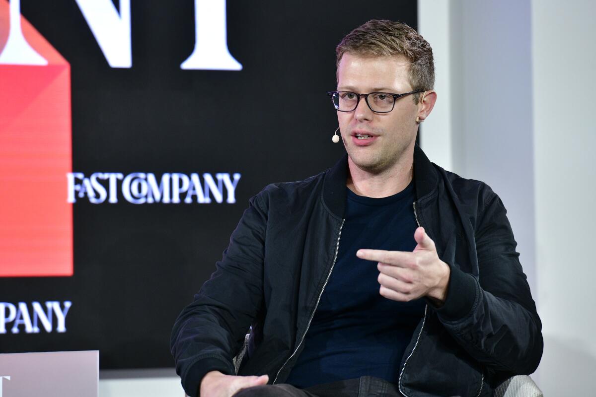 CEO Grant LaFontaine gestures while speaking onstage with a headset microphone; behind him, the Fast Company logo