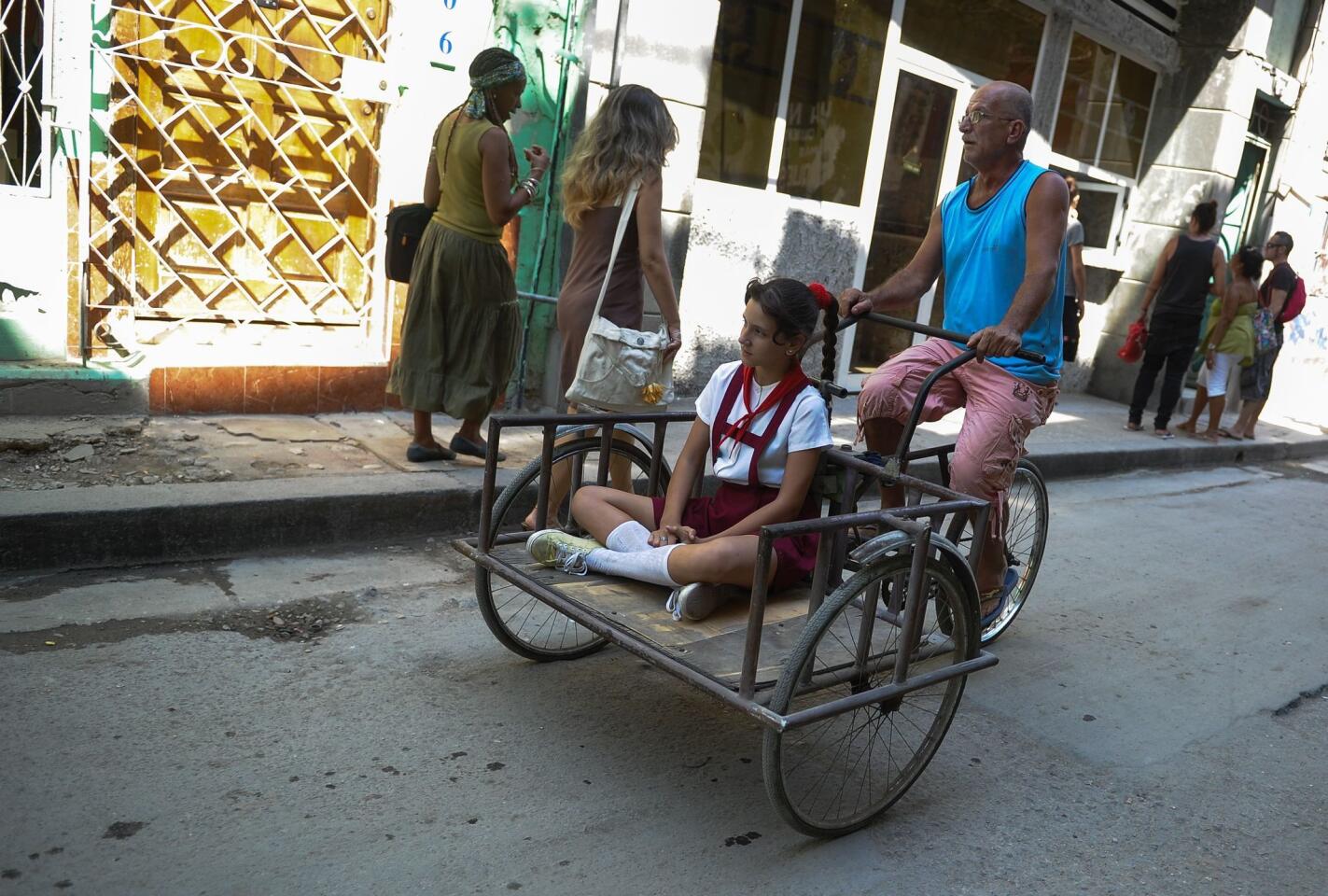 A man rides a tricycle with a child along a street of Havana on March 17, 2016.