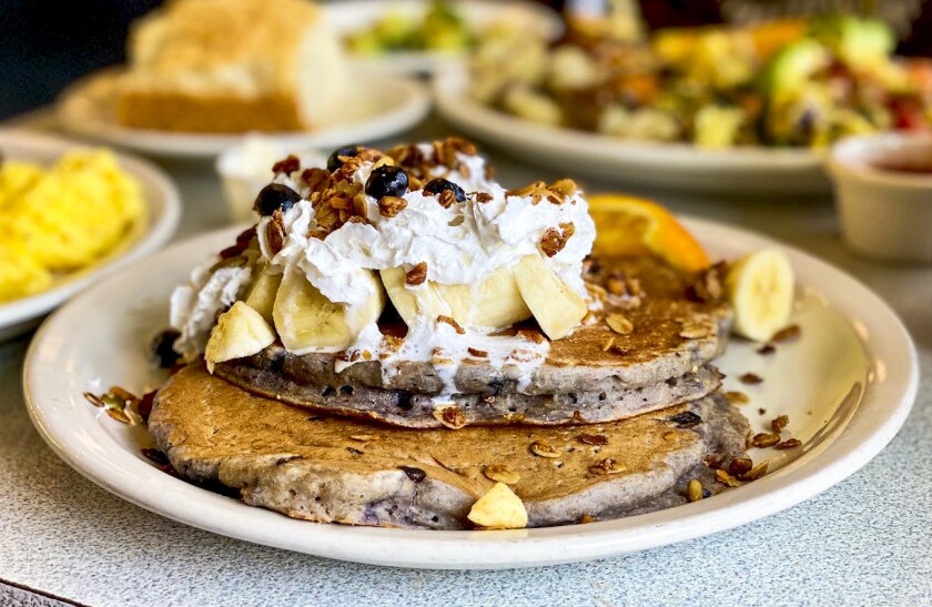 Pancakes on a plate topped with sliced banana, whipped cream, granola and berries.