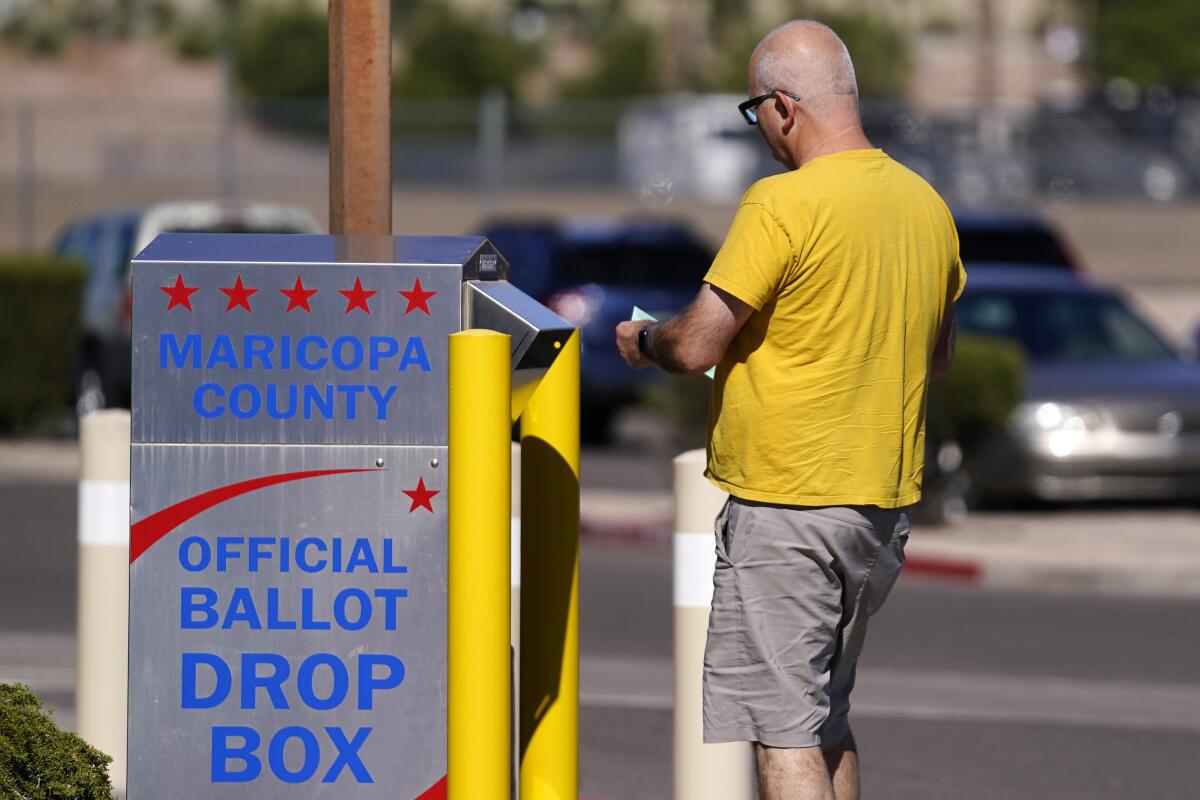 A man holding a ballot and walking up to a tall box outside labeled "Maricopa County Official Ballot Drop Box."