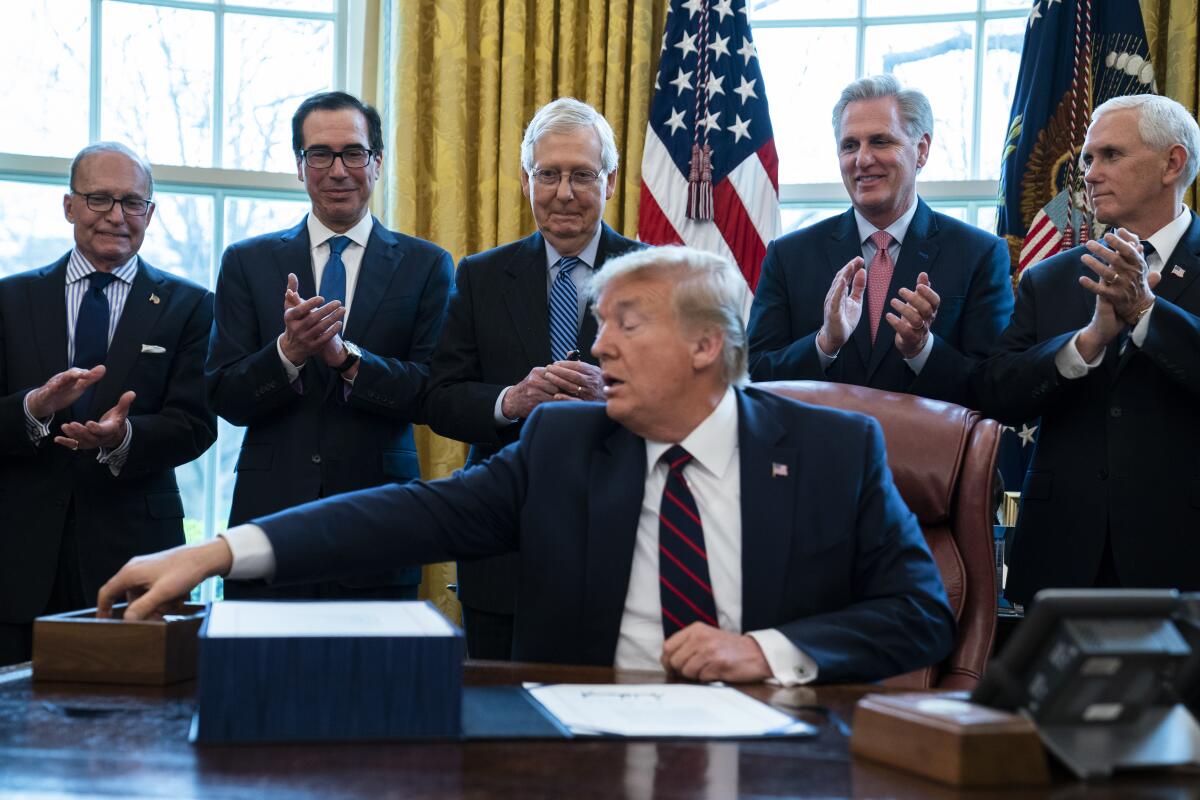 Surrounded by White House aides and GOP congressional leaders, President Trump signs the $2-trillion bailout bill Friday. From left, White House chief economic advisor Larry Kudlow, Treasury Secretary Steven T. Mnuchin, Senate Majority Leader Mitch McConnell (R-Ky.), House Minority Leader Kevin McCarthy (R-Bakersfield) and Vice President Mike Pence.