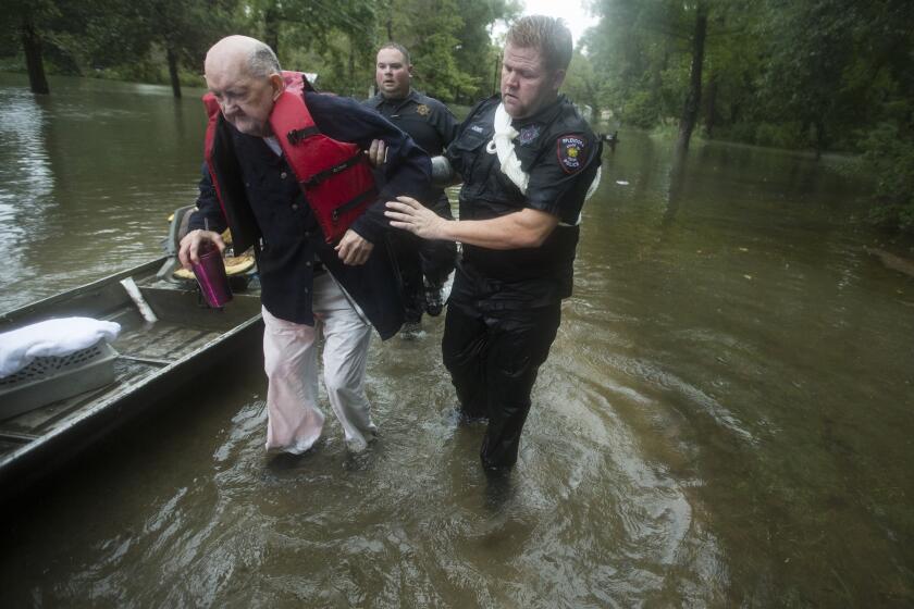 Fred Stewart, left, is helped to high ground by Splendora Police officer Mike Jones after he was rescued from his flooded neighborhood as rains from Tropical Depression Imelda inundated the area, Thursday, Sept. 19, 2019, in Splendora, Texas. (Brett Coomer/Houston Chronicle via AP)