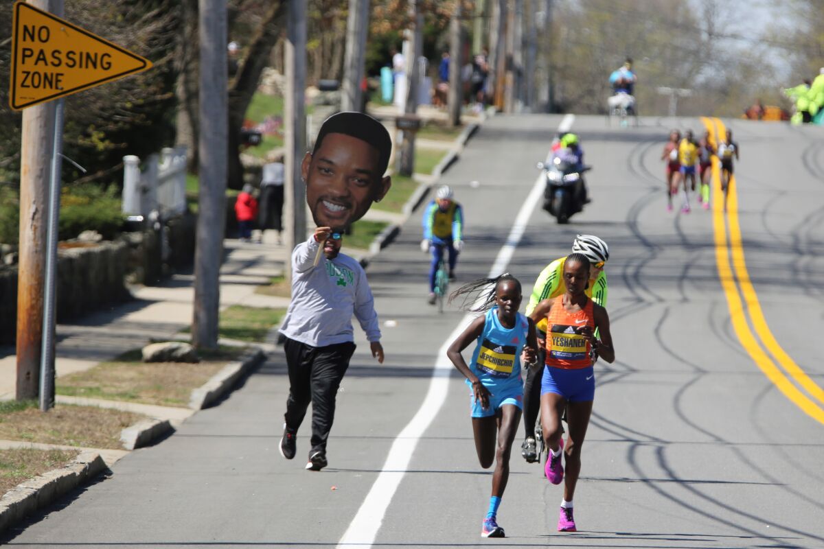 A man carrying a picture of actor Will Smith runs behind Peres Jepchirchir, of Kenya, left, and Ababel Yeshaneh, of Ethiopia, during the 126th Boston Marathon in Natick, Mass, Monday, April 18, 2022. (AP Photo/Jennifer McDermott)