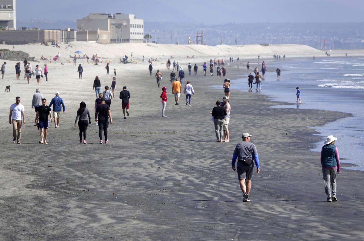 People walk along the beach in Coronado, which is among the few remaining beaches open in San Diego County on March 29, 2020.