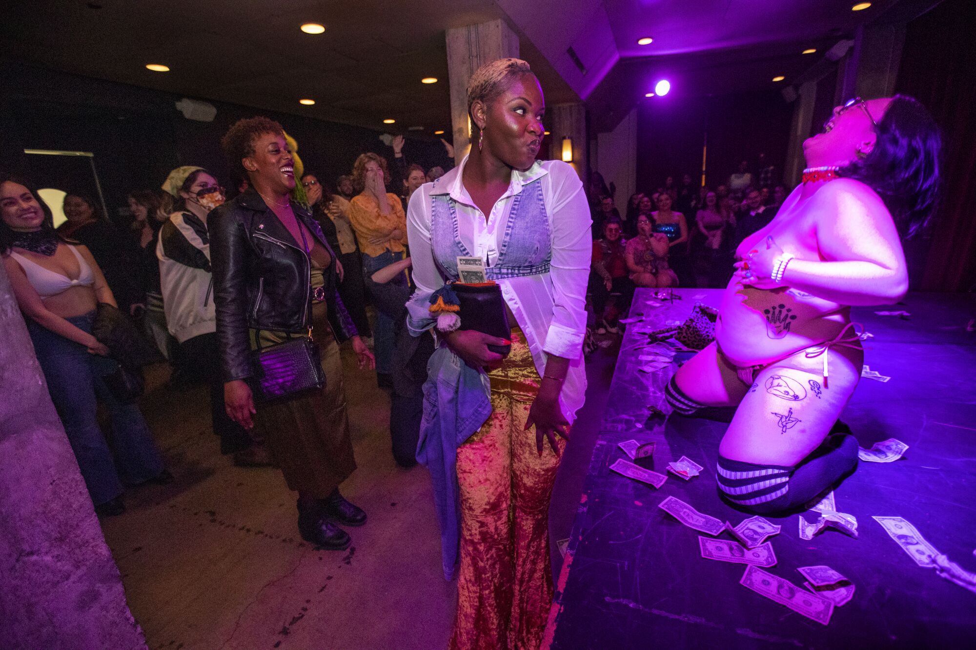 A burlesque performer kneels onstage and throws back her head to laugh.