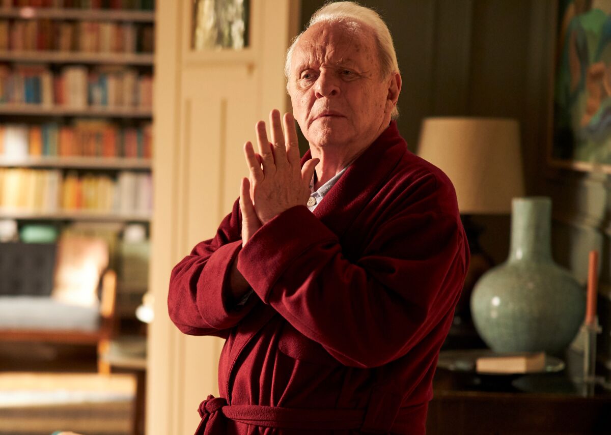 Anthony Hopkins, in a red bathrobe with his palms pressed together