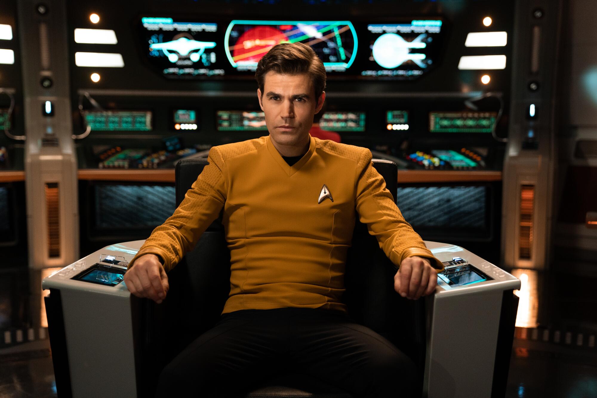 James T. Kirk sits in a chair on a spaceship with lit screens displayed behind him.