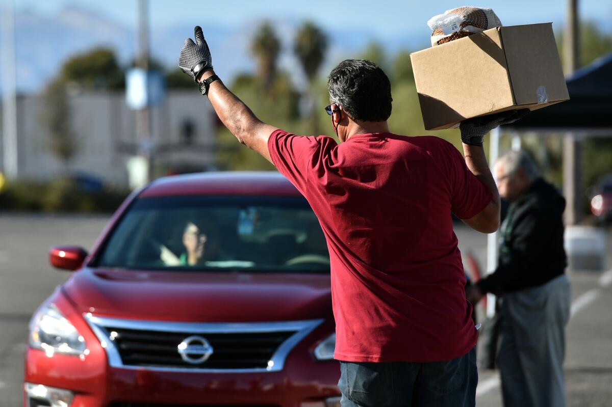 Greg Arce carries a Thanksgiving dinner for distribution during the Fall Giving Pop-Up as a car drives up.