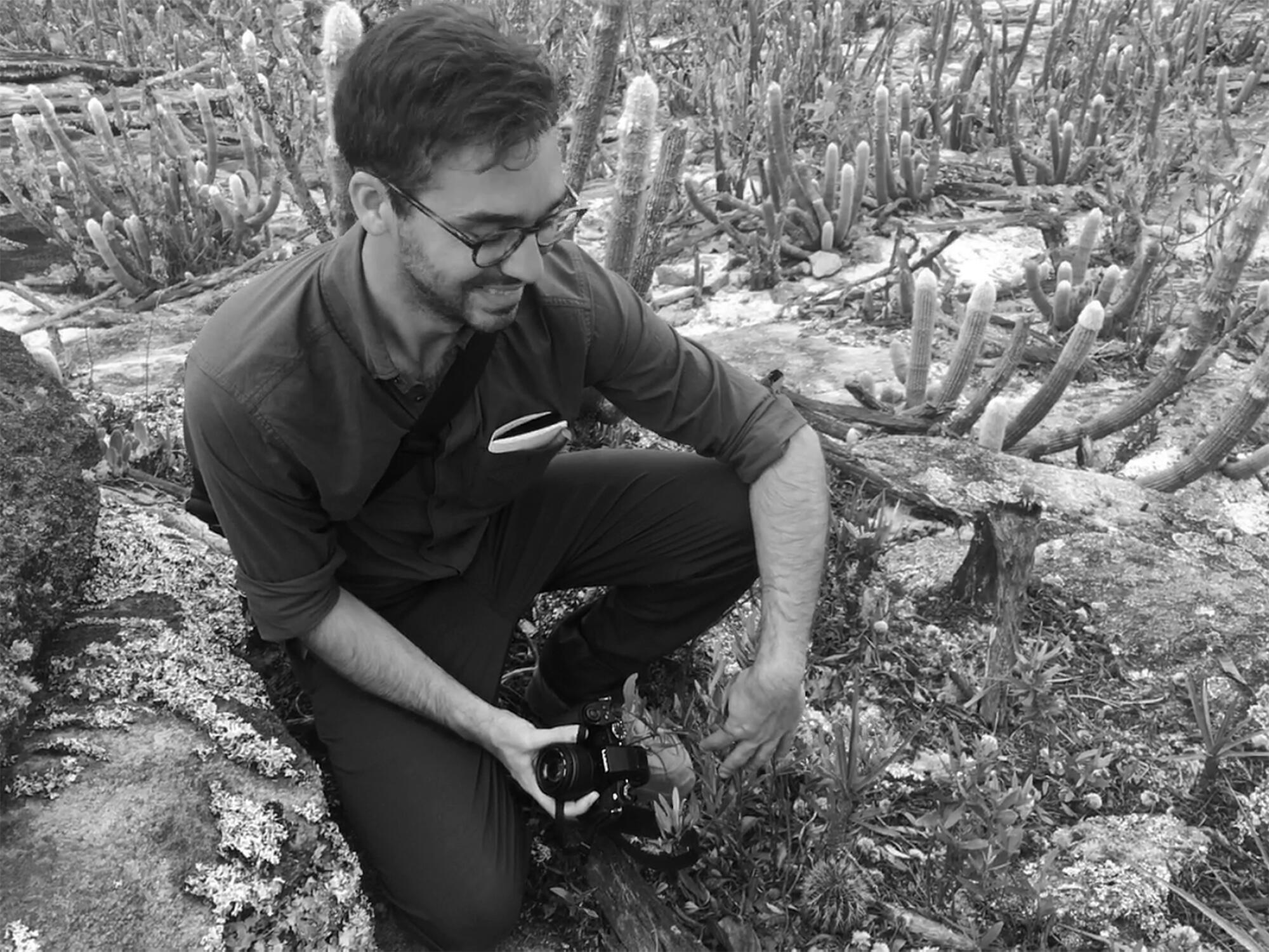 A man with a camera in his hand looking down at a rare, small species of cactus.