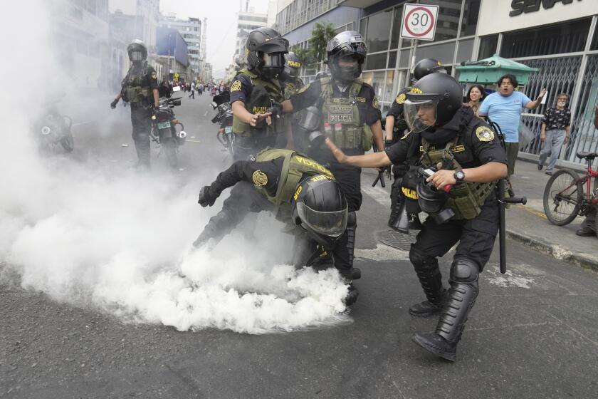 Police officers pick up a tear gas canister that was thrown back at them by anti-government protesters who traveled to the capital from across the country to march against Peruvian President Dina Boluarte in Lima, Peru, Wednesday, Jan. 18, 2023. Protesters are seeking immediate elections, Boluarte's resignation, the release of ousted President Pedro Castillo and justice for the dozens of protesters killed in clashes with police. (AP Photo/Martin Mejia)