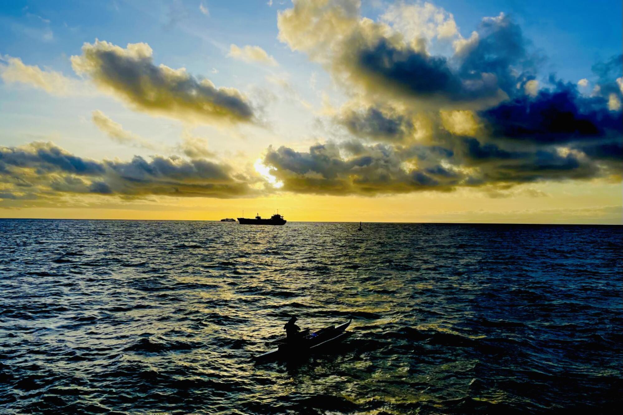 A fisherman navigates an outrigger in the waters off Dumaguete, under large clouds near dusk.