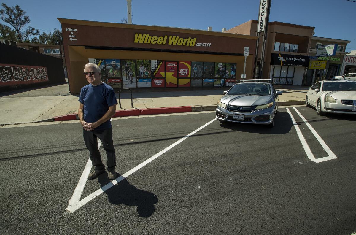 A man stands in the street between newly painted parking space lines in front of a retail shop.