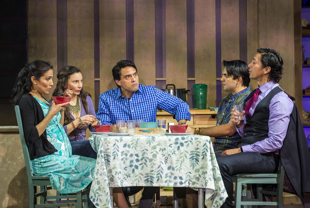A group of actors sit around a dinner table in a tense moment in a scene from a play 