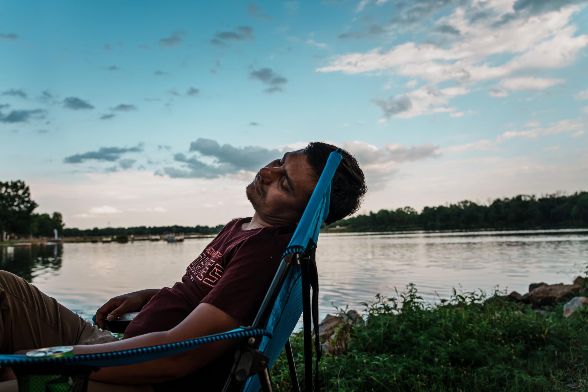 Man relaxes in chair with a lake and blue skies as a backdrop 