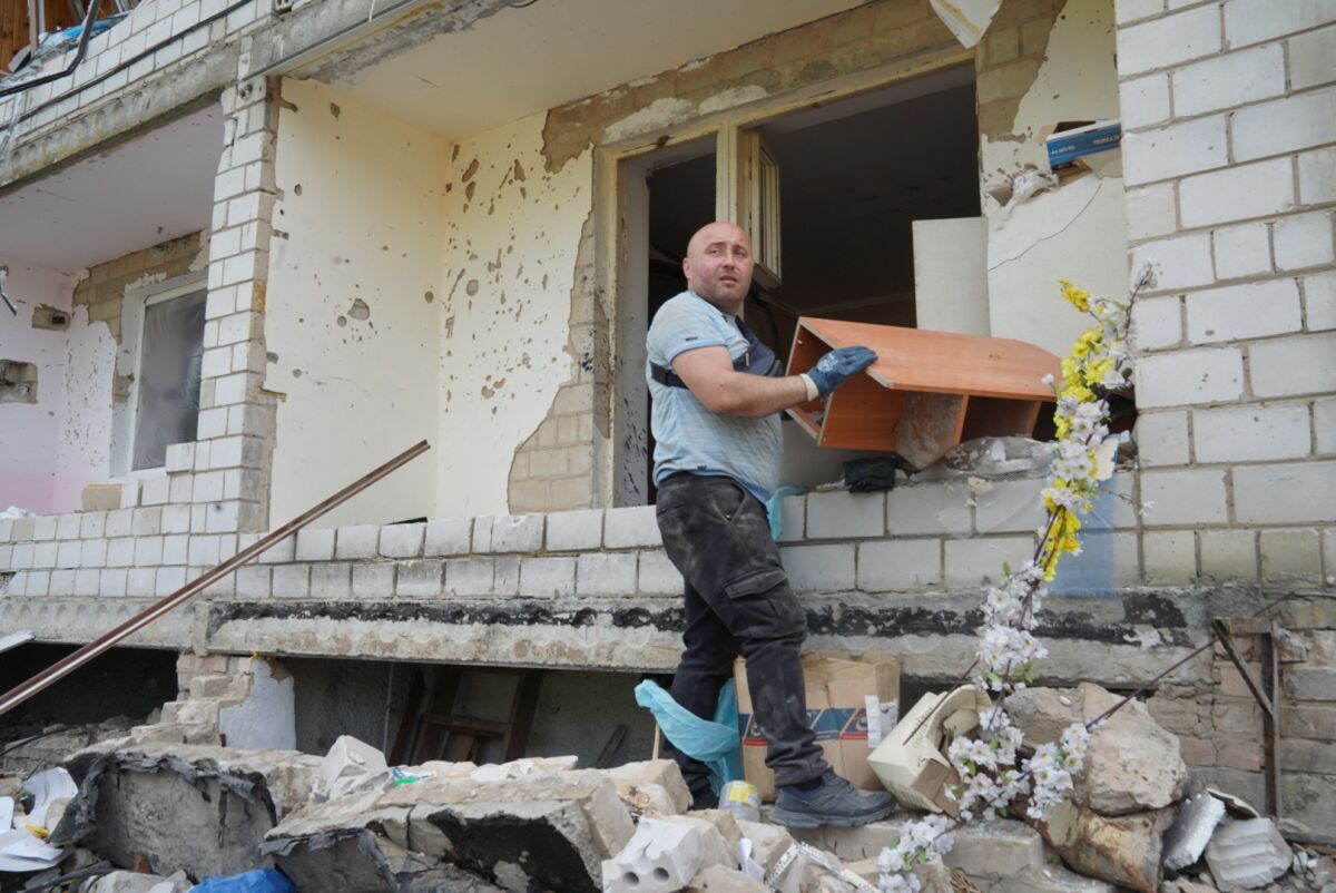 A man pulls a shelf through a window of a bombed-out apartment building.