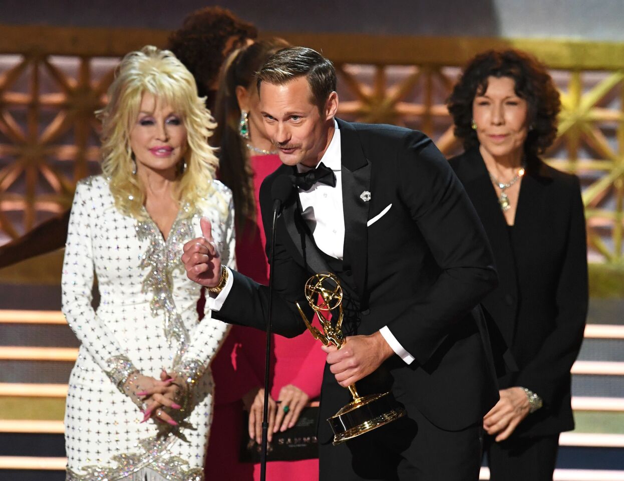 Actor Alexander Skarsgard accepts for supporting actor in a limited series or movie for "Big Little Lies" with Dolly Parton, left, and Lily Tomlin during the 69th Emmy Awards.