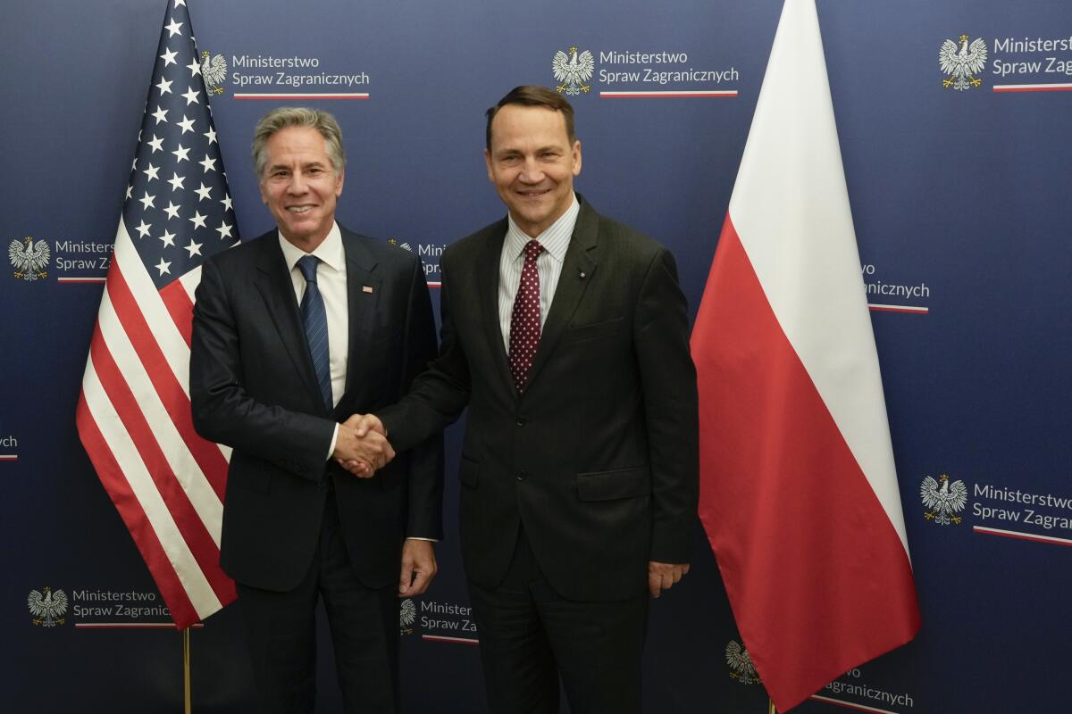 Antony Blinken and Radek Sikorski shake hands between U.S. and Polish flags