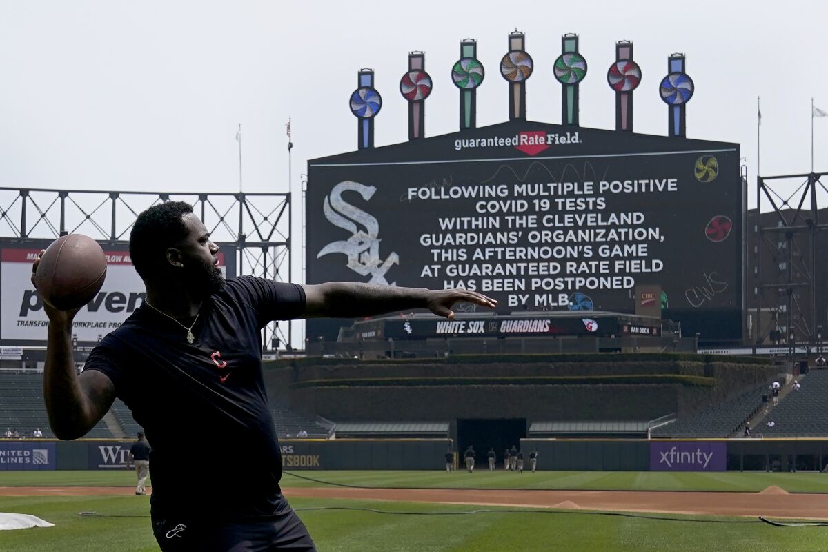 Cleveland Guardians' Franmil Reyes throws a football to teammate Myles Straw as the scoreboard informs fans that the baseball game between the Chicago White Sox and the Guardians has been postponed due to multiple positive COVID-19 tests within the Guardians organization, Wednesday, May 11, 2022, in Chicago. (AP Photo/Charles Rex Arbogast)