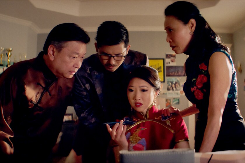 Two men and a women stand around a woman sitting down holding up a cellphone