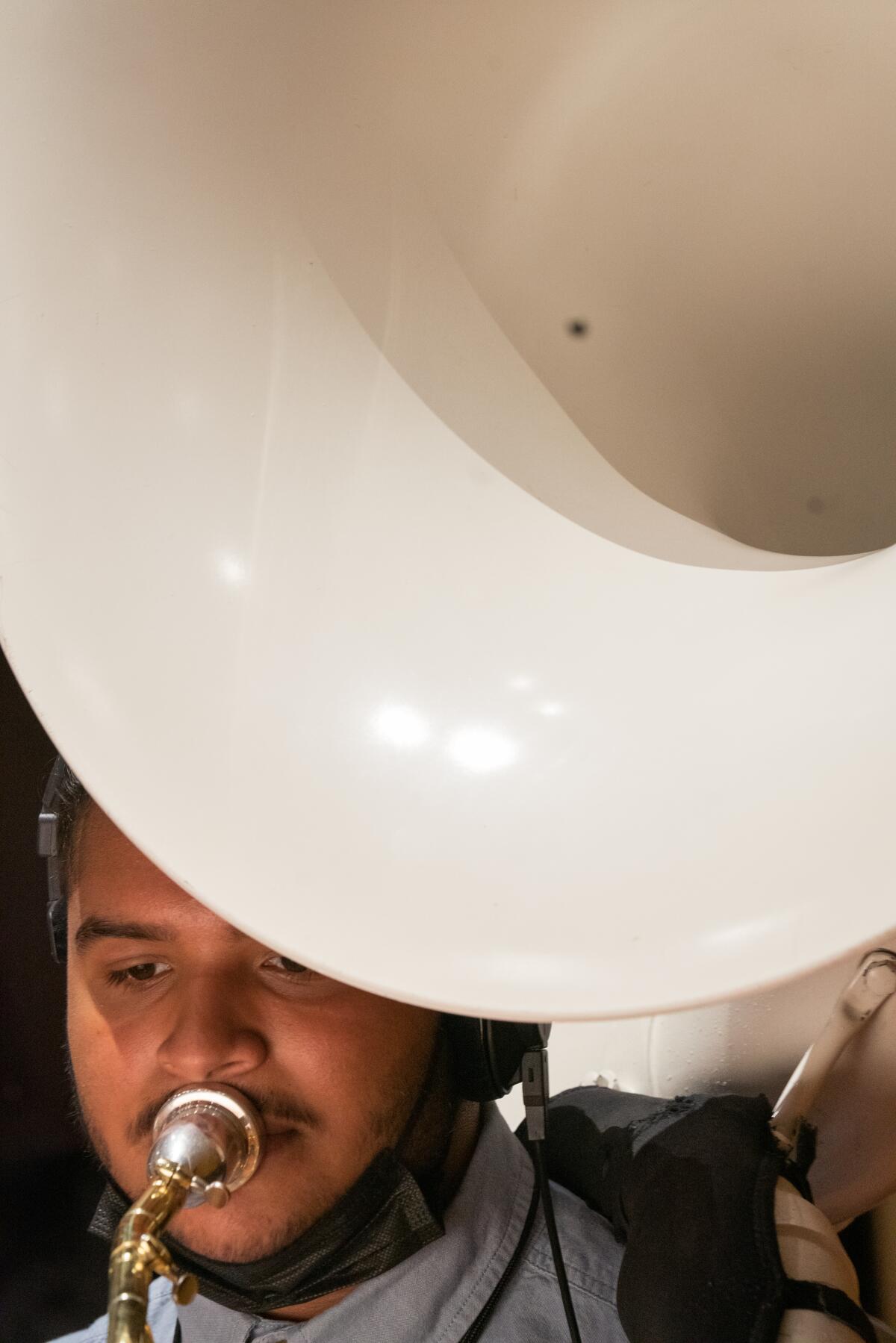 A teenager is seen in a close-up portrait playing the sousaphone.
