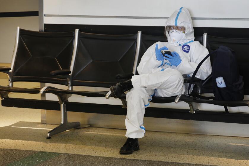 LOS ANGELES, CA - MAY 11: One of several students returning home to China after studying in the U.S. wears a protective suit while waiting for a flight at the Tom Bradley International Terminal, Los Angeles International Airport (LAX) which is now requiring travelers to wear face covering to help keep fellow passengers and crew safe by limiting the spread of the coronavirus Covid-19. The students said they will all wear the same suit but will don the suit after passing thorough security. The new requirements for wearing face masks in Los Angels began Monday at LAX and on local public transit. LAX on Monday, May 11, 2020 in Los Angeles, CA. (Al Seib / Los Angeles Times)