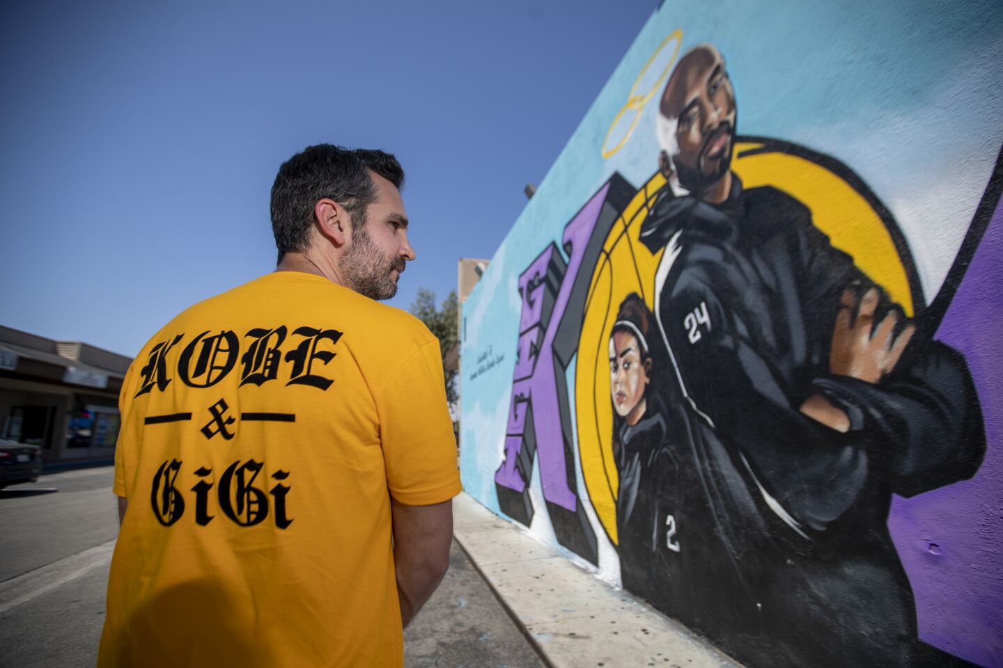 Mike Asner, creator of the KobeMural Instagram maps and Kobemural.com, shows off the back of his T-shirt, standing in front of Tyke Witnes' mural at El Toro Bravo Meat Market in Costa Mesa.