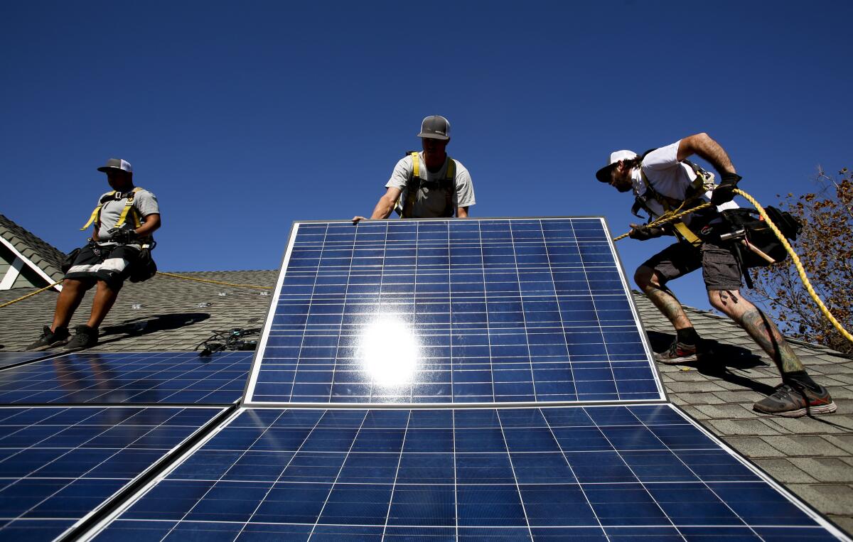 Workers install solar panels on the roof of a home.