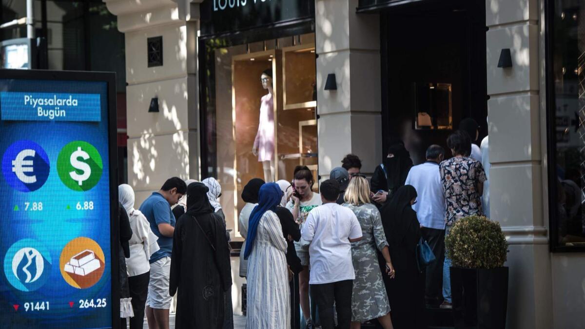 Tourists, many from Saudi Arabia and Asia, stand in line outside a Louis Vuitton store in Istanbul, Turkey, next to a digital billboard giving updates on various currencies on Aug. 13.