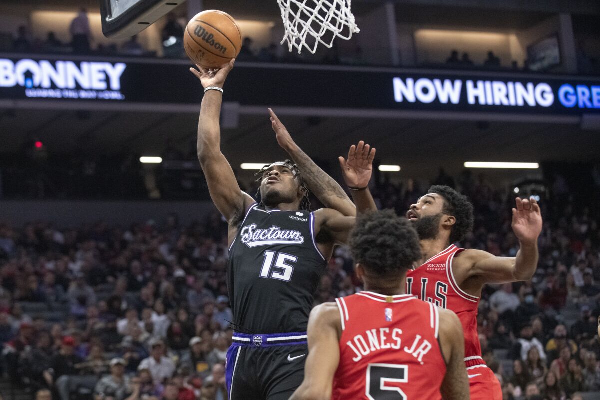 Sacramento Kings guard Davion Mitchell (15) drives to the basket as Chicago Bulls forward Derrick Jones Jr. (5) and guard Coby White defend during the first quarter of an NBA basketball game in Sacramento, Calif., Monday, March 14, 2022. (AP Photo/Randall Benton)