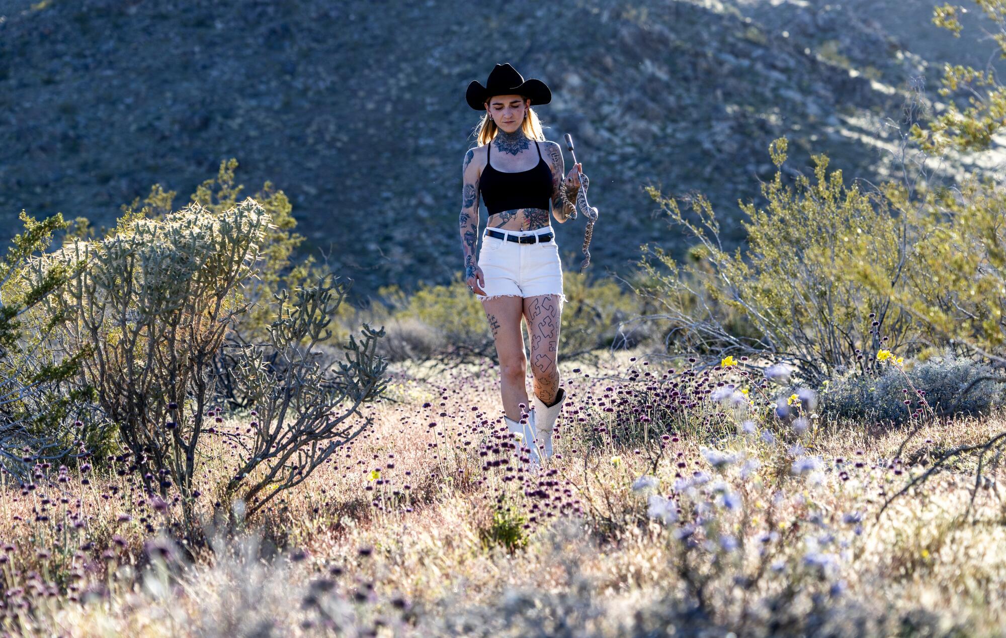 Danielle Wall walks through the desert scrubland on her property with a rattlesnake