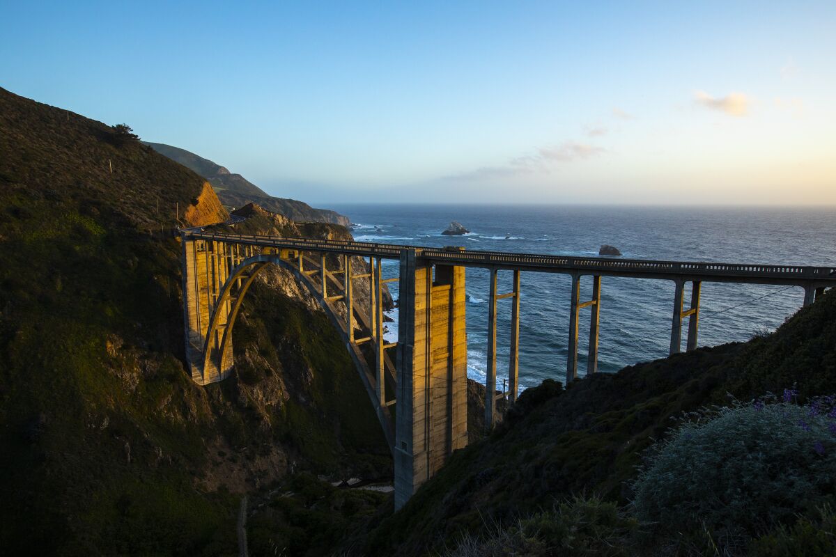 A bridge over a canyon with the Pacific Ocean in the background.