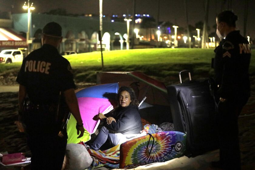 VENICE, CA - JULY 8, 2021 - - L.A.P.D. officers ask a homeless woman if she would like housing before saying that she could not camp at the site as sanitation crews clear homeless encampments along Ocean Front Walk around 3:15 a.m. in Venice on July 8, 2021. The homeless woman declined housing, packed up and walked away with her belongings. Sanitation crews, working alongside L.A.P.D. officers and workers with St. Joseph Center, were clearing encampments between Windward Ave. and Park Ave along the boardwalk. (Genaro Molina / Los Angeles Times)