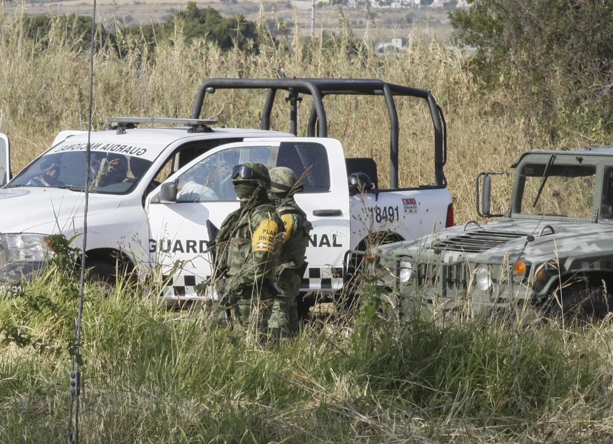 Soldiers stand guard in a grassy area near a white truck and a jeep 