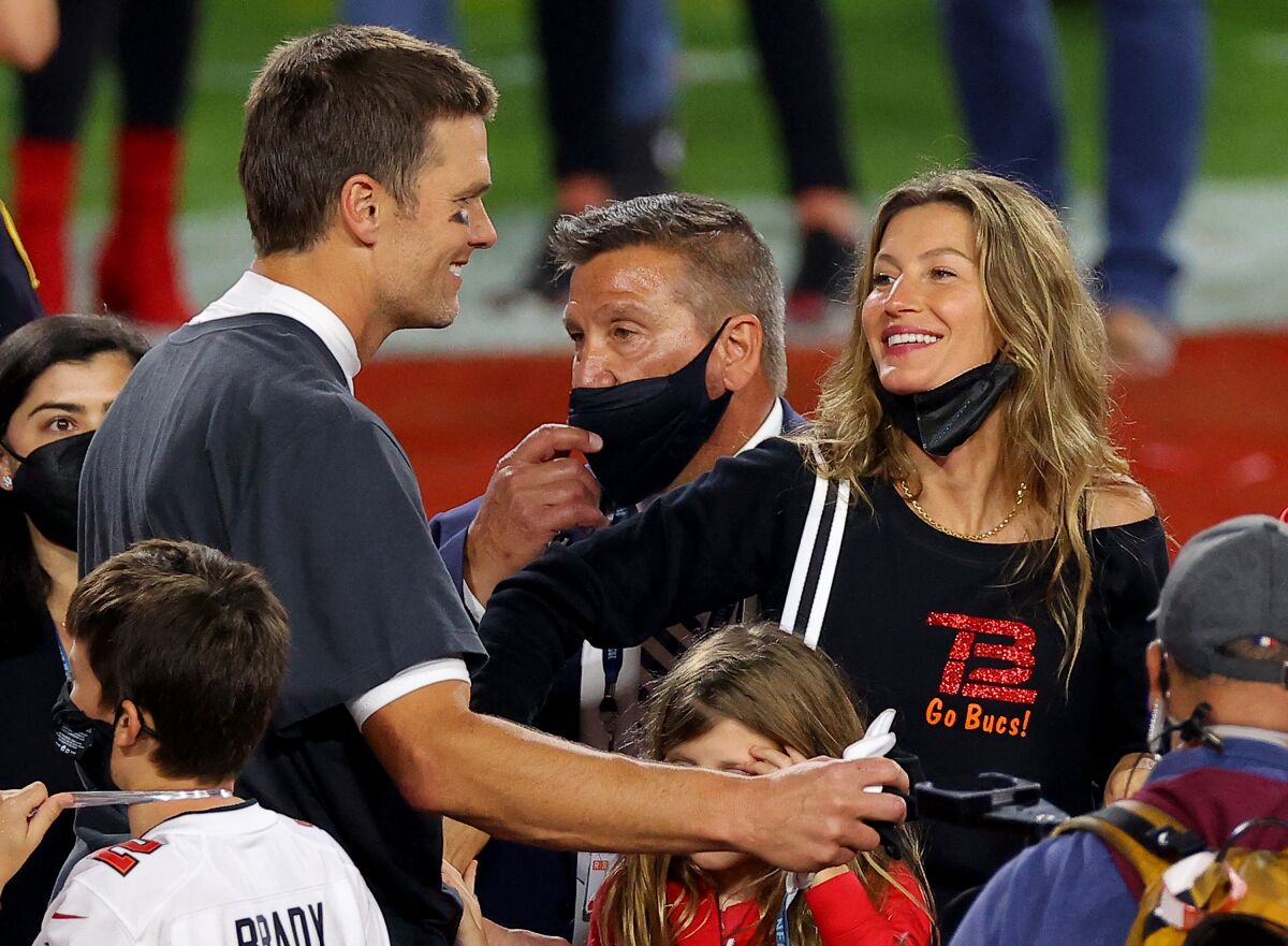 A beautiful football player and a beautiful model smile at each other amid a crowd of people on a football field