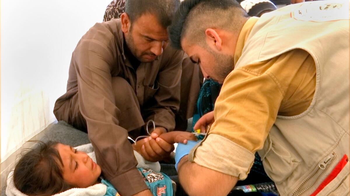 A man comforts his daughter as a doctor treats her after she was taken ill with suspected food poisoning on Tuesday in the Hassan Sham U2 camp near Mosul, Iraq.