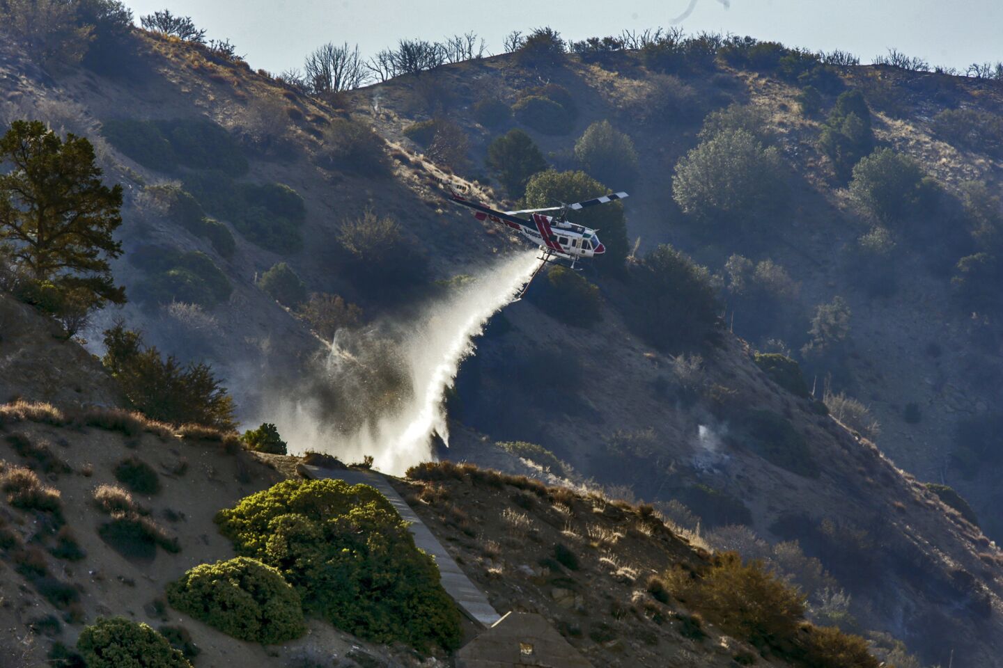A CalFire helicopter makes a water drop on still smoldering remnants of Blue Cut Fire on the hilltop ridges along Hwy 2 in Wrightwood.