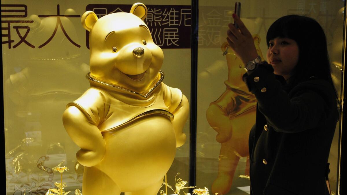 A woman takes a photo beside a gold sculpture of Winnie the Pooh in an outlet of Chow Tai Fook Jewellry in Chengdu, China, on March 23, 2012.