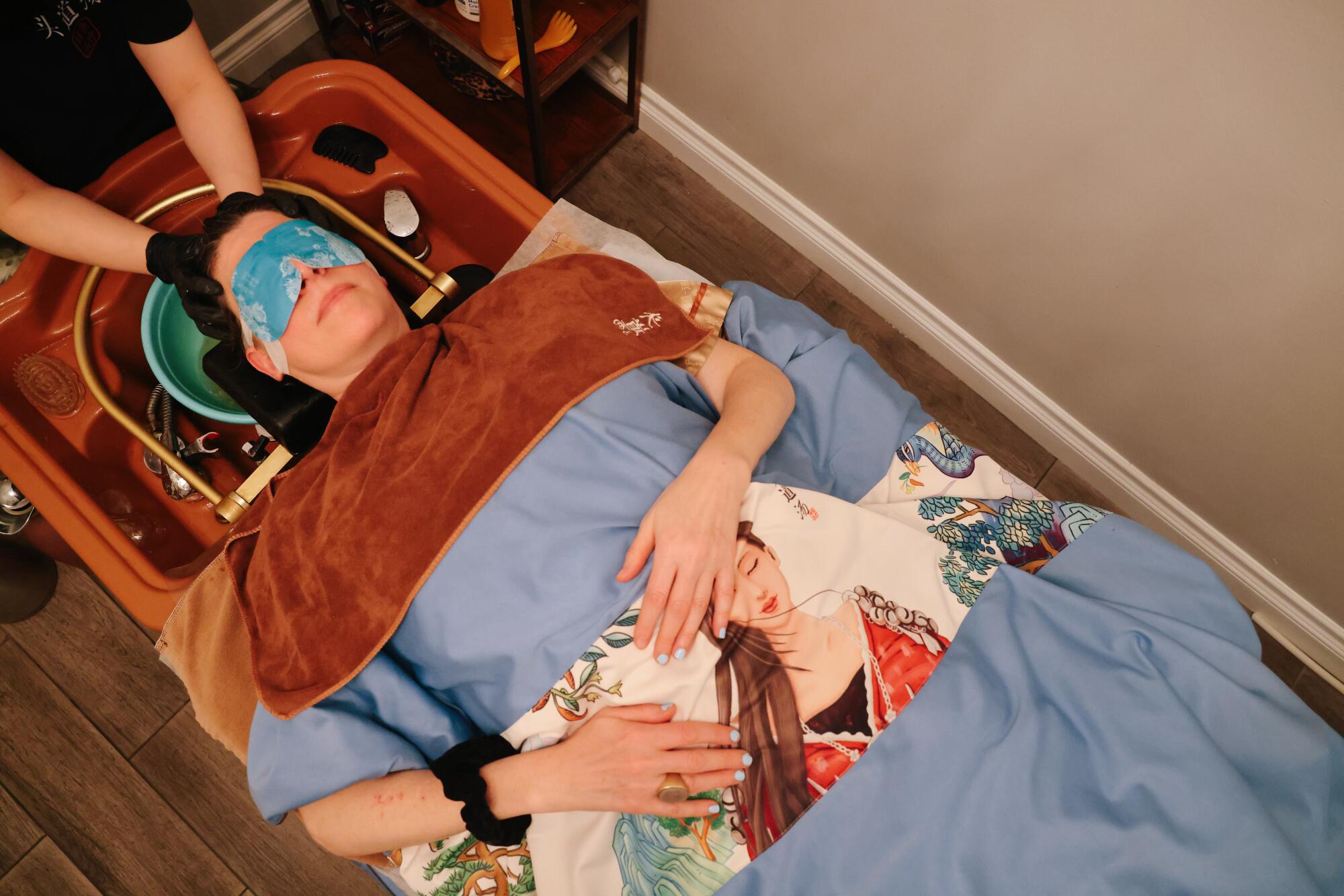 A masked woman receives a Chinese scalp treatment from Tou Dao Tang head spa.