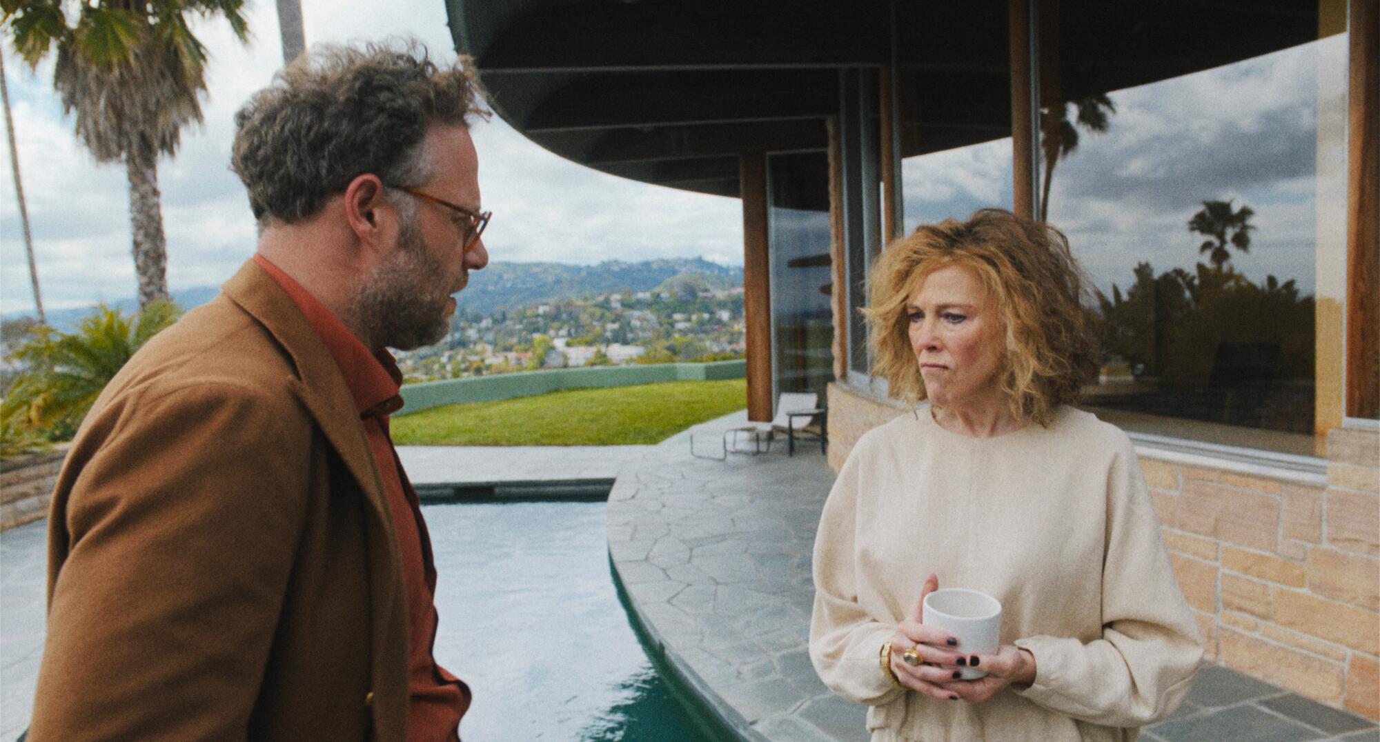 A man and a woman stand outside a house with a curved facade and a reflecting pool overlooking Los Angeles