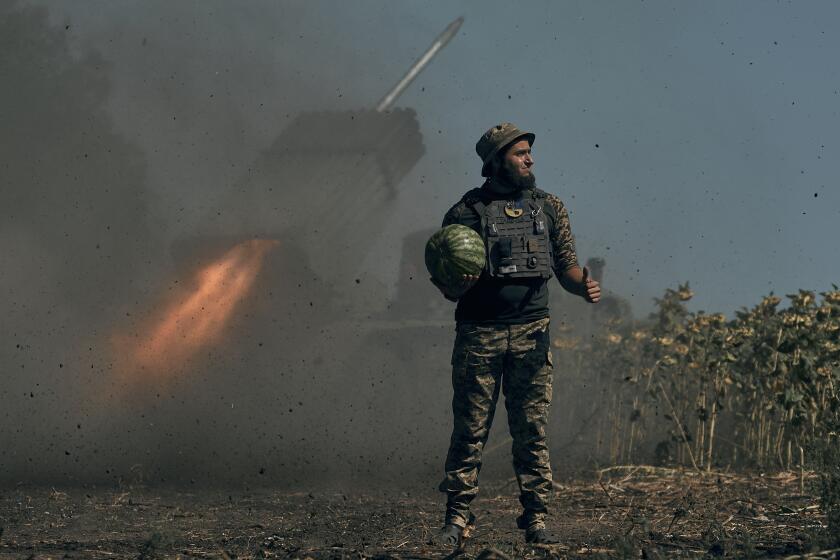 A Ukrainian soldier holds a watermelon and thumbs up as a rocket launch system fires in the font line in Donetsk region, eastern Ukraine, Saturday, Aug. 3, 2022. (AP Photo/Kostiantyn Liberov)