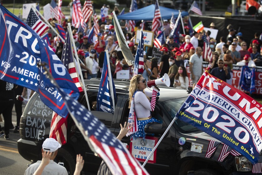 Trump and U.S. flags wave as a woman with a megaphone leans out of an SUV with the words "Galactics for Trump" on it