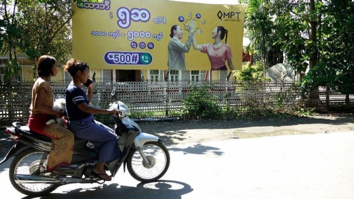Two women ride past an ad for a cellphone company in Sittwe, Myanmar. The Myanmar government has temporarily shut down internet access in several conflict zones.