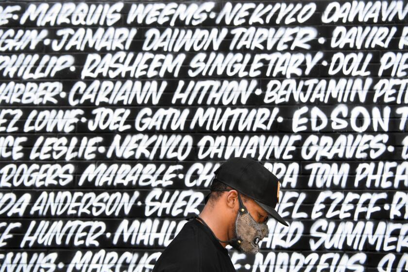 HOLLYWOOD, CALIFORNIA JUNE 6, 2020-A protestor honors the names on a Black Lives Matter mural on Fairfax Ave. during a march Saturday. The protest was organzied by the Refuse Fascism group. (Wally Skalij/Los Angeles Times)