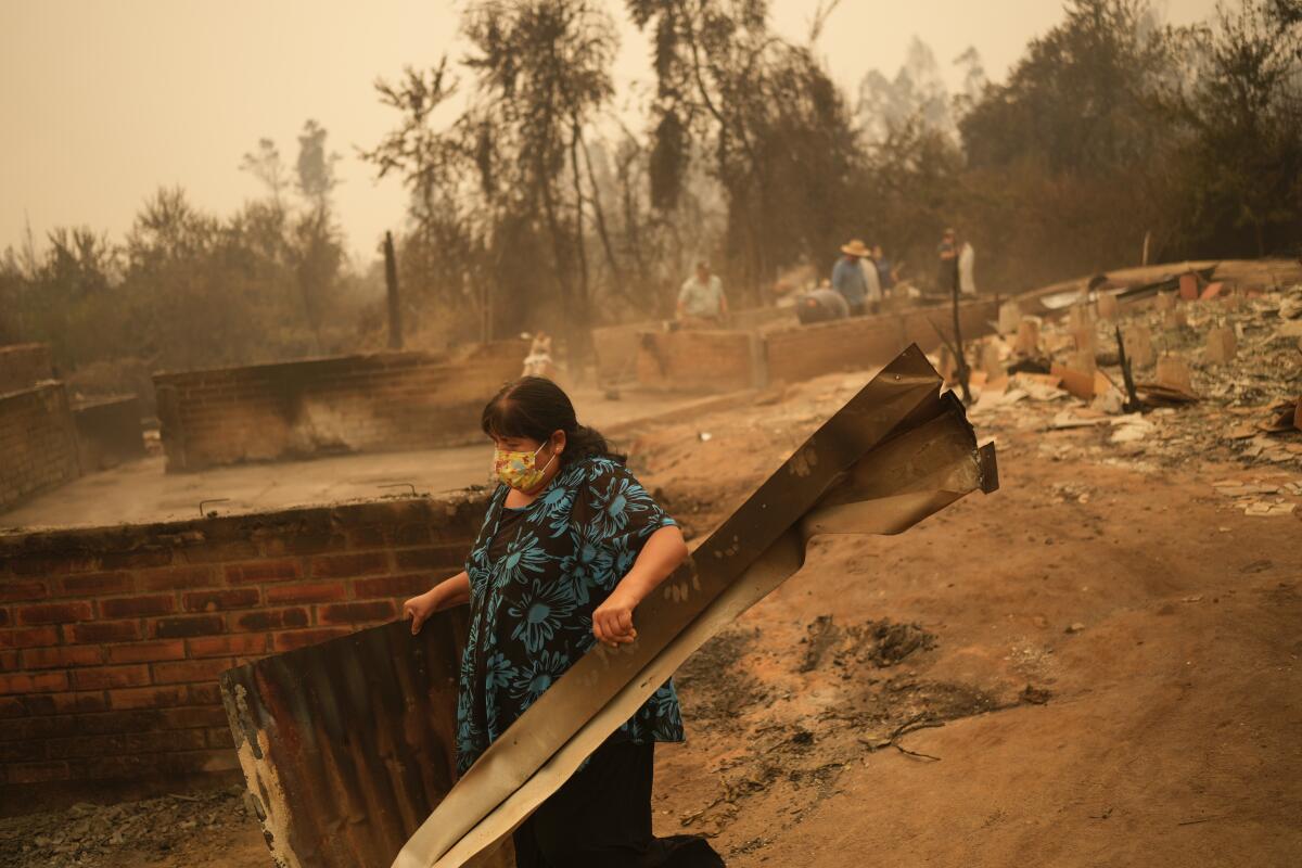 A woman wearing a mask clears debris amid a charred landscape