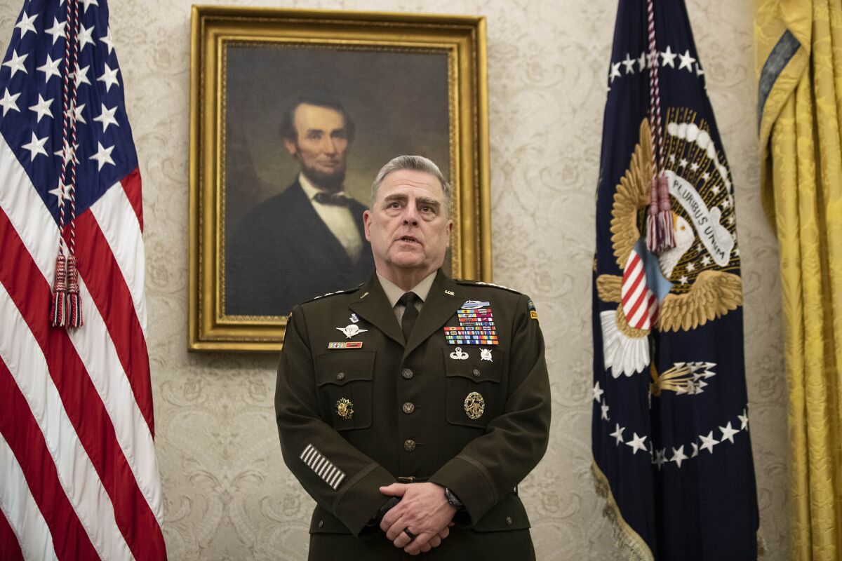A general in dark military uniform, flanked by U.S. flags, stands in front of a portrait of Abraham Lincoln 