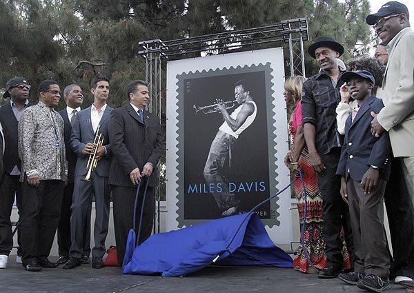 The unveiling of the Miles Davis stamp by Eduardo H. Ruiz Jr., left, L.A. District manager of the USPS, and Miles Davis' daughter Cheryl Davis, right, and musicians and members and friends of the Davis family during the U.S. Postal Service dedication of the Miles Davis stamp before the concert.
